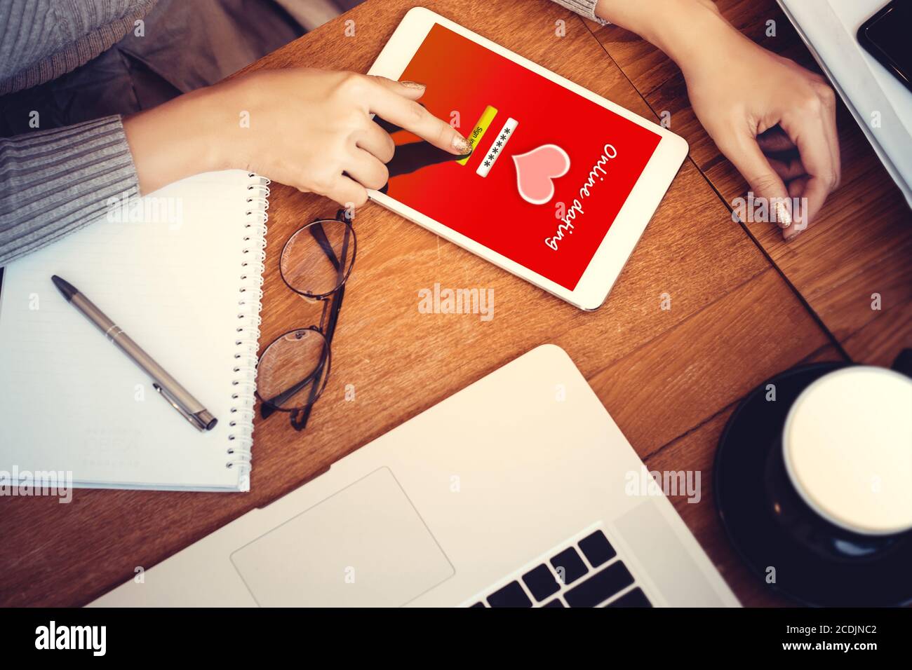 online love concept: girl using a digital generated tablet with dating site on the screen, hardwood desktop and stationery on background Stock Photo
