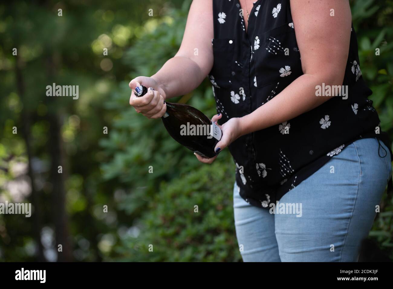 A woman pops a bottle of champagne open at a graduation party Stock Photo