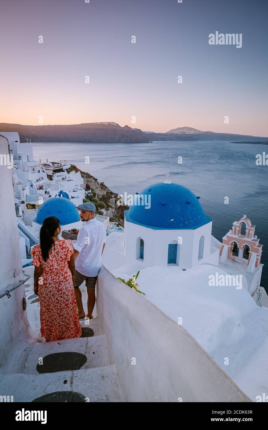 Santorini Greece, young couple on luxury vacation at the Island of Santorini watching sunrise by the blue dome church and whitewashed village of Oia Stock Photo