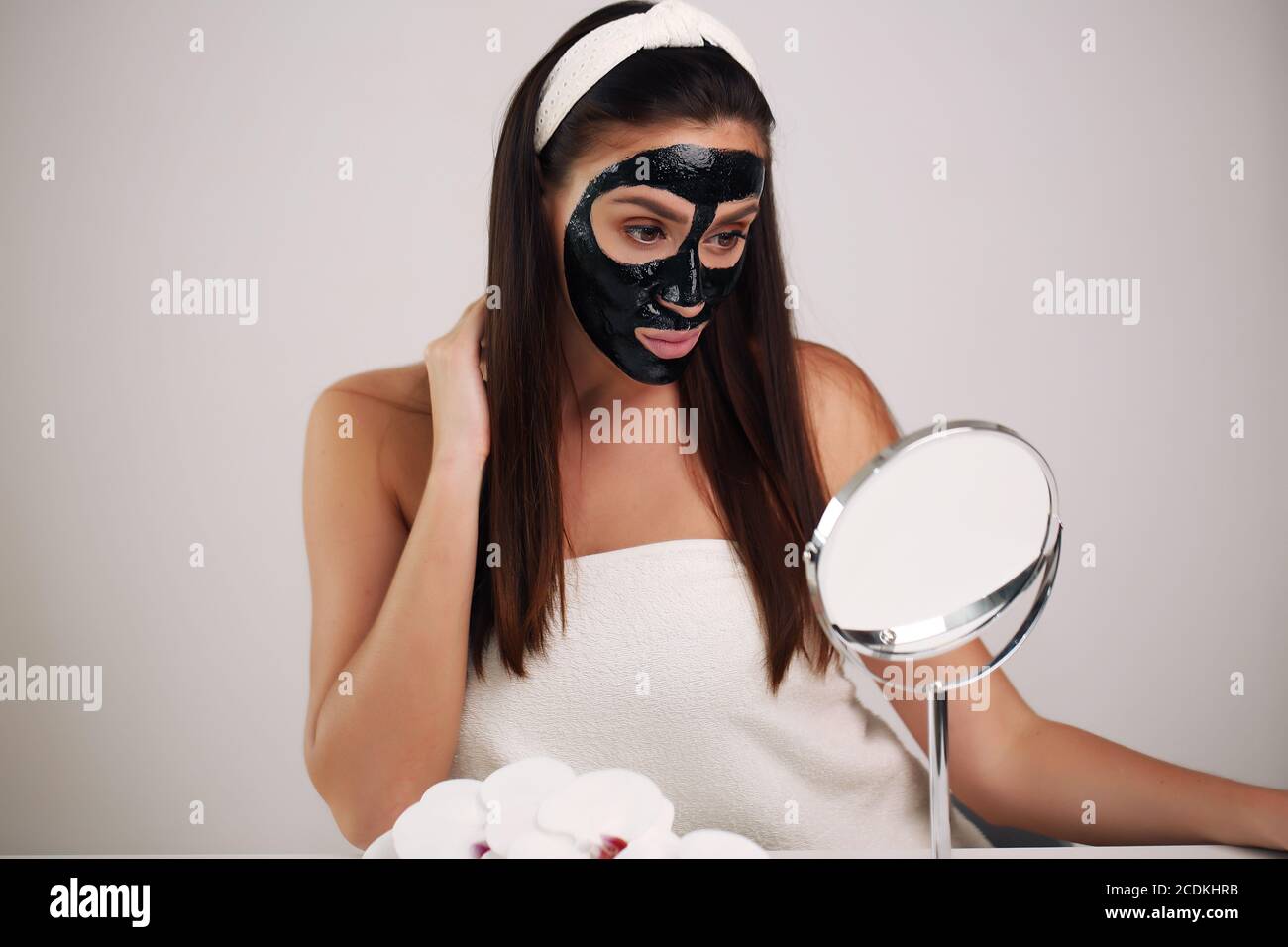 Young woman with carbon detox black mask on face, teenage girl takes care of oily skin, cleansing pores. Beauty salon. Skin care. Stock Photo