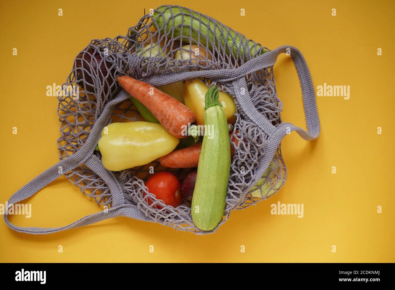 Gray bag string bag with vegetables,zucchini,bell peppers,carrots,beets,onions yellow background.Harvest from garden fresh bright vegetables.Concept z Stock Photo