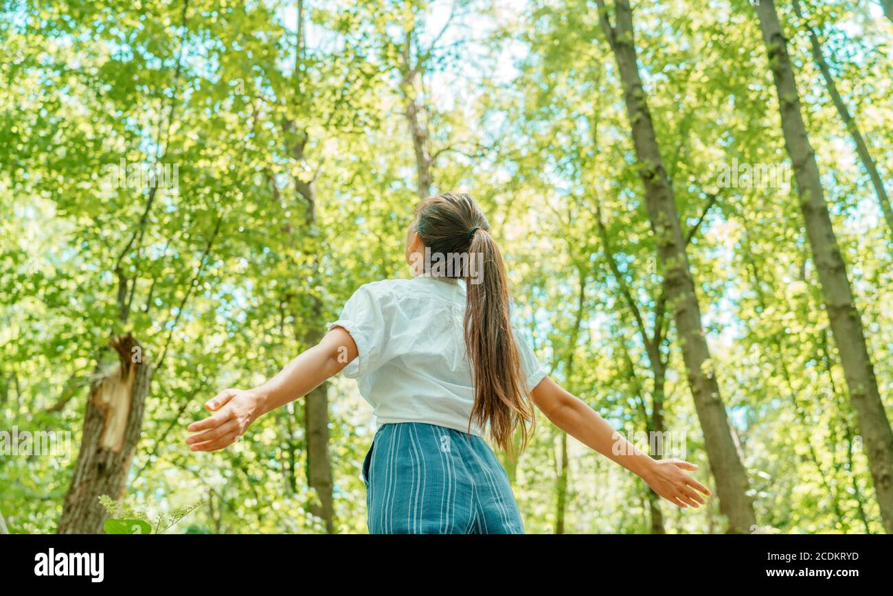Free woman breathing clean air in nature forest. Happy girl from the back with open arms in happiness. Fresh outdoor woods, wellness healthy lifestyle Stock Photo