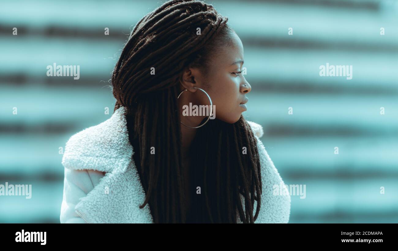 Profile of an adorable young black female with big dreadlocks, round earrings, and piercing in her nose, she is looking aside while standing outdoors Stock Photo