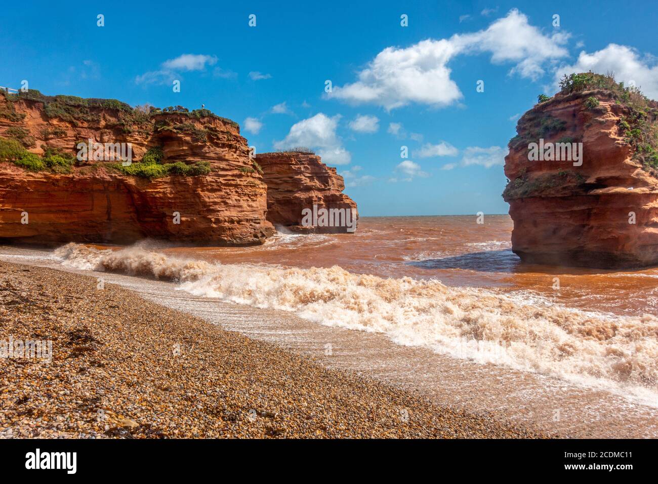 Waves roll onto the beach at Ladram Bay in South Devon, England. Sandstone cliffs have eroded over time to leave a free standing stack Stock Photo