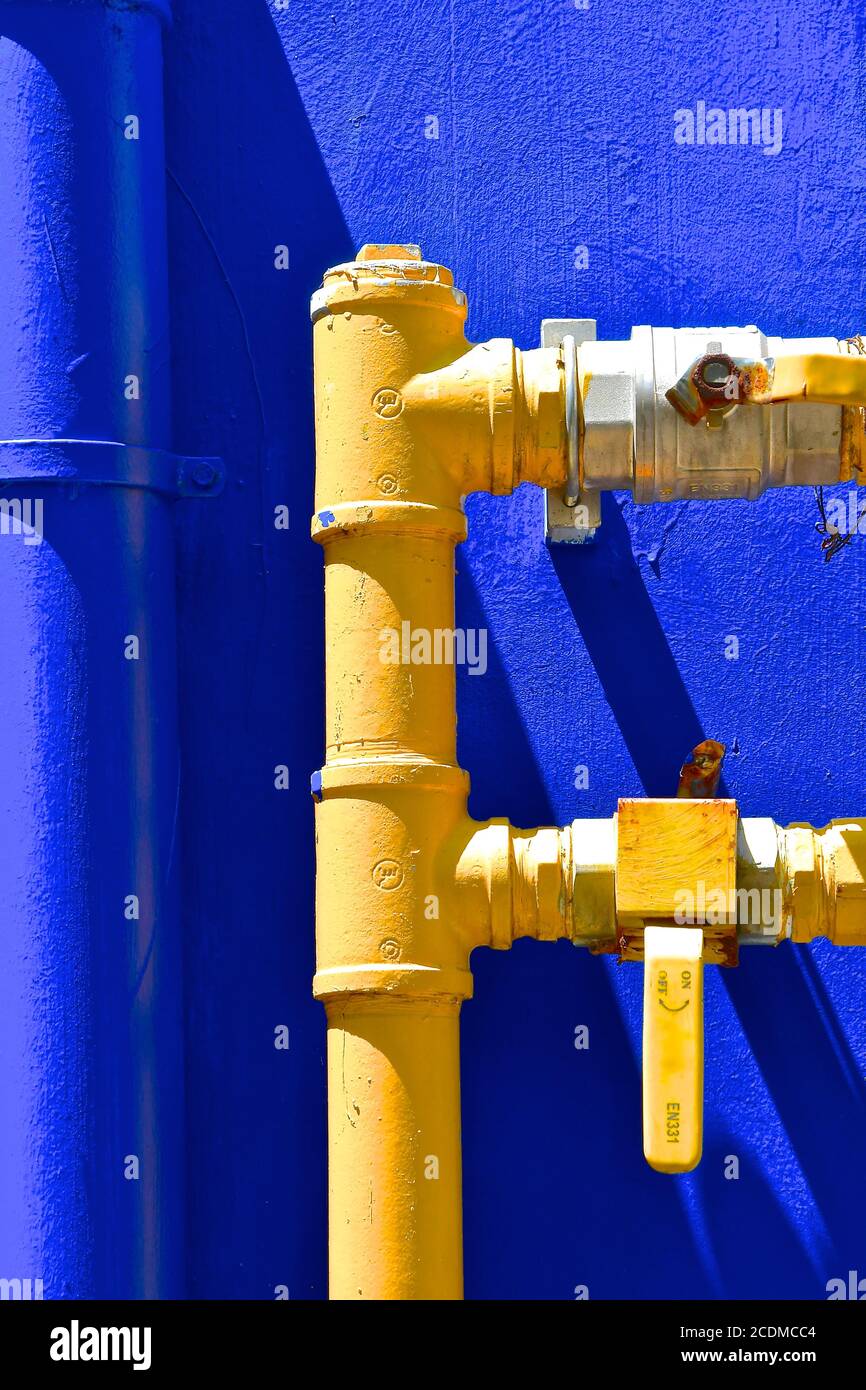 Heavy duty industrial yellow, metal water pipes and taps, isolated against a dark blue background. Stock Photo