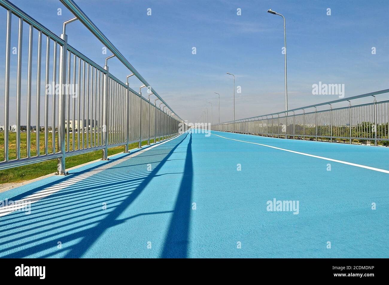 Perspective view of a blue cycle track with stainless steel fencing and a blue sky background, lines showing the vanishing point. Stock Photo
