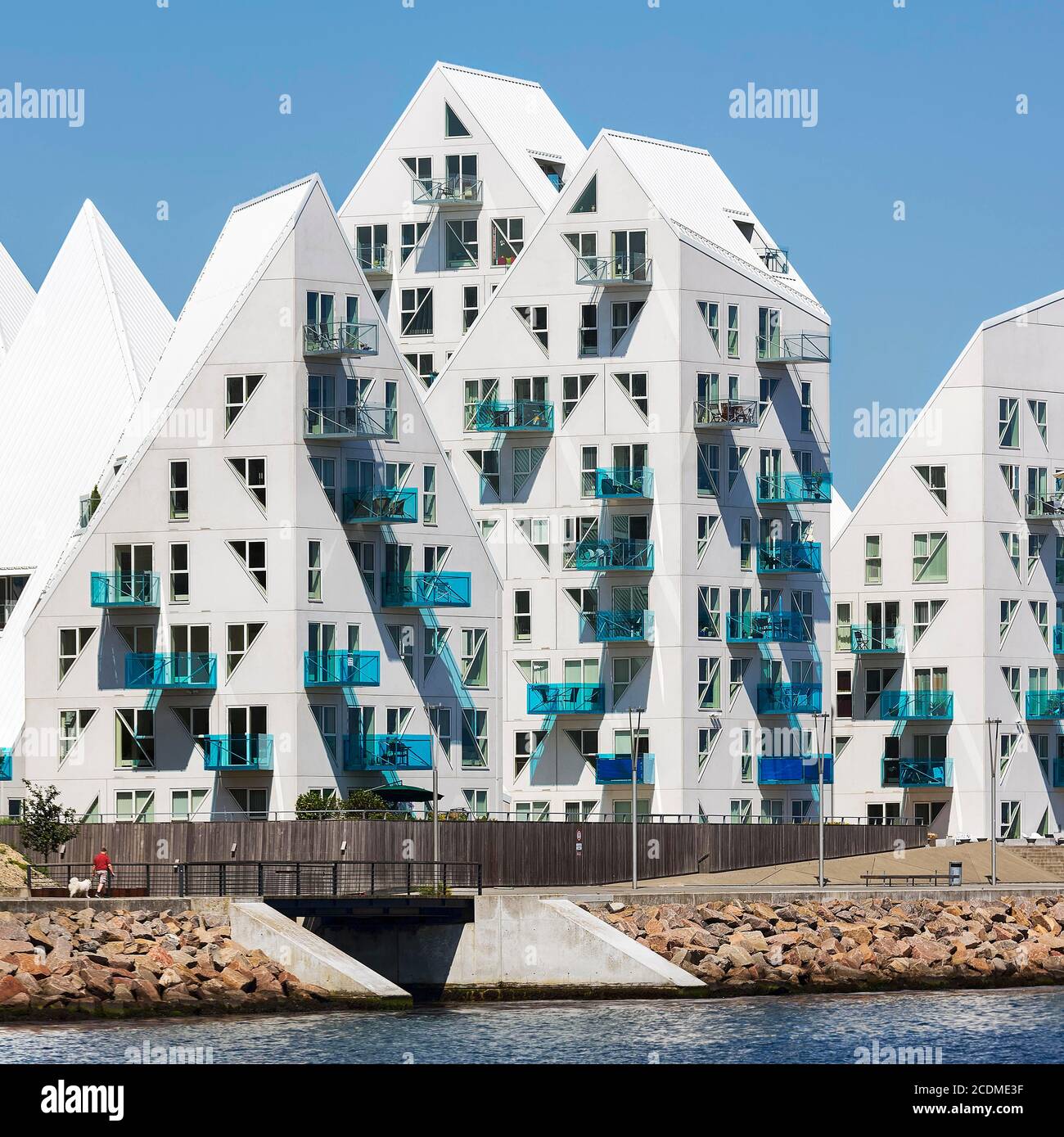 White residential complex with turquoise balconies by the sea, jagged building sculpture Isbjerget in front of blue sky, iceberg, modern architecture Stock Photo