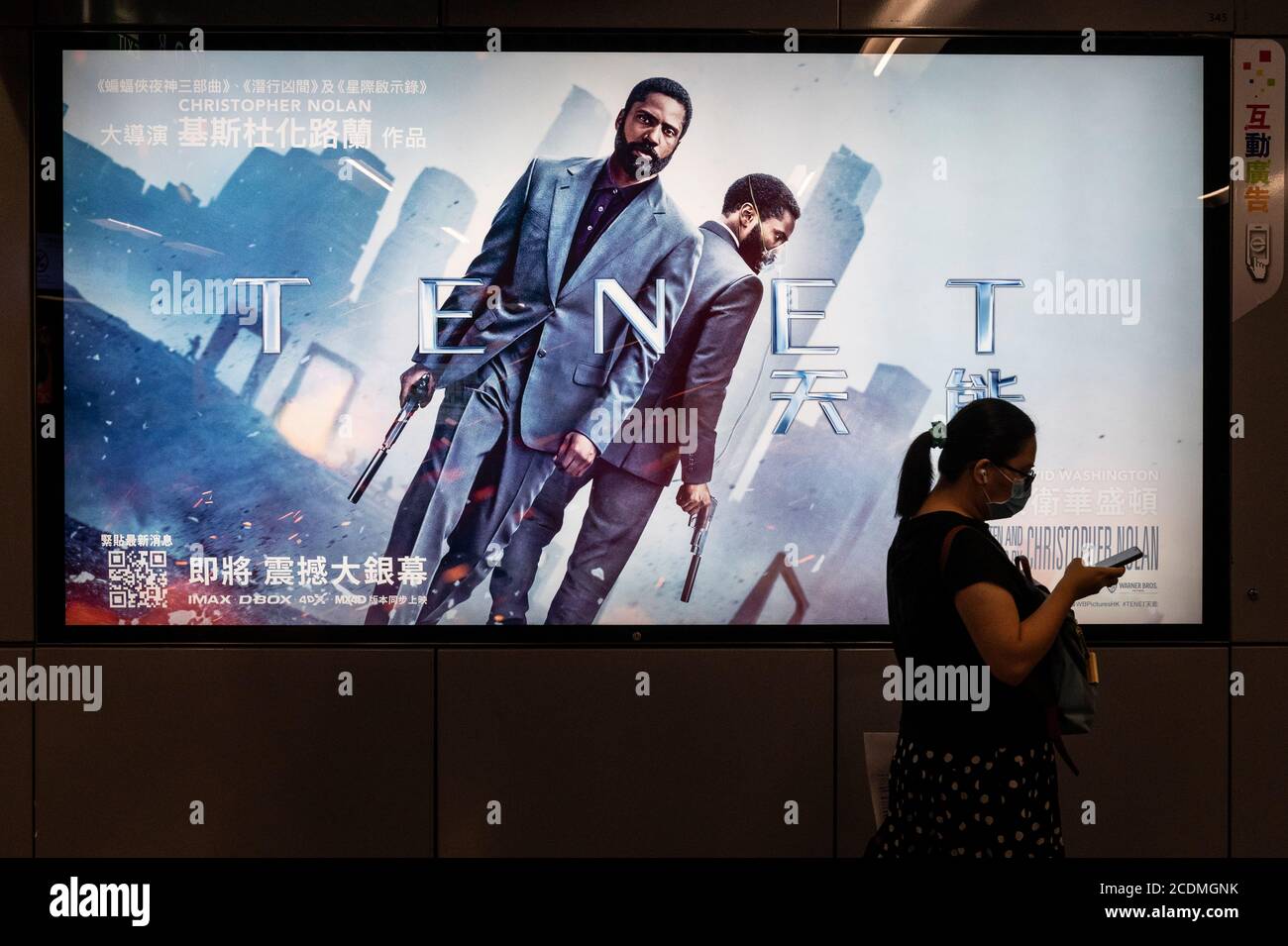 A commuter walks past a poster of Christopher Nolan's blockbuster film Tenet at MTR subway station in Hong Kong. Stock Photo