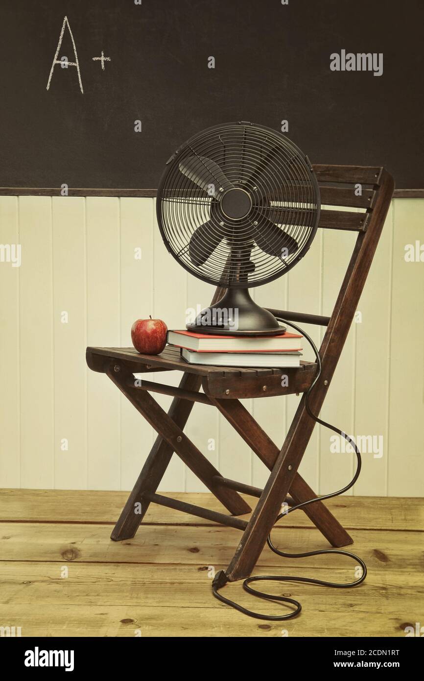 Old fan with apple and books on chair in school ro Stock Photo