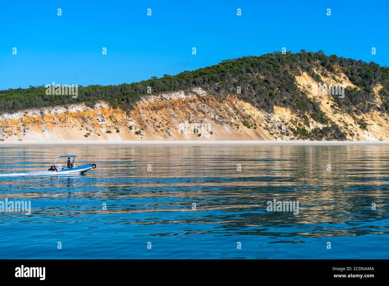Small boat speeding along western shore of Fraser Island with coloured dunes in background Stock Photo