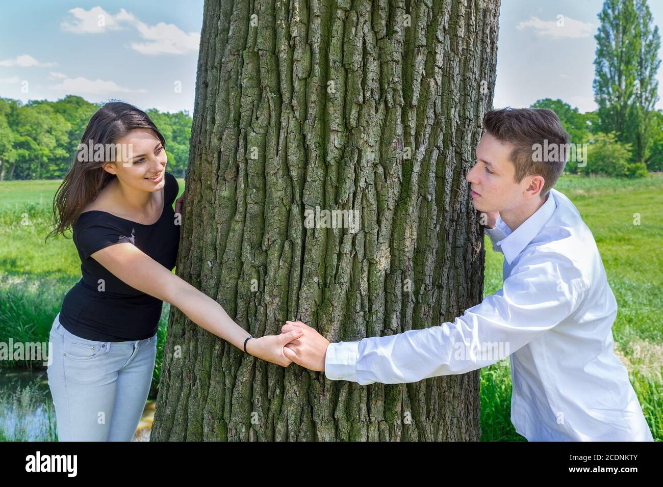 Young attractive caucasian couple in love holding hands around tree trunk Stock Photo