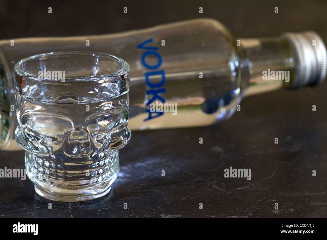 Alcohol kills. Bottle of vodka and glass in shape of skull on dark background, alcohol addiction concept Stock Photo