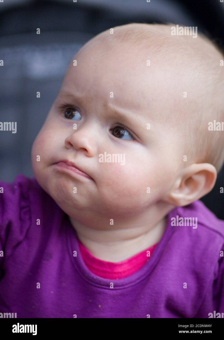 A frowning baby wearing a purple top in a pram Stock Photo