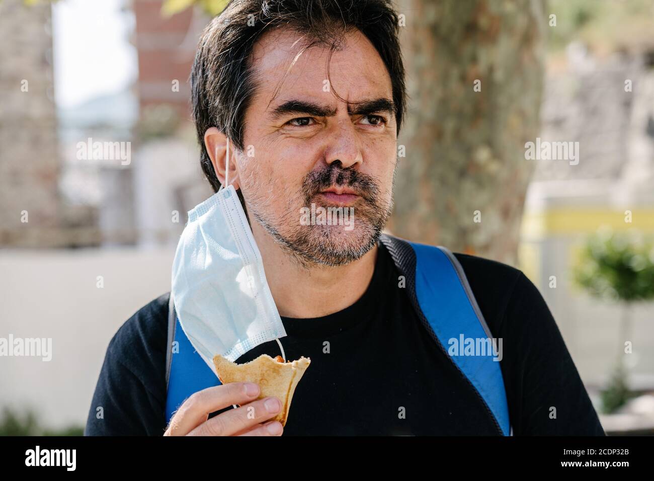 Adult male eating a snack with the removed face mask hanging from his