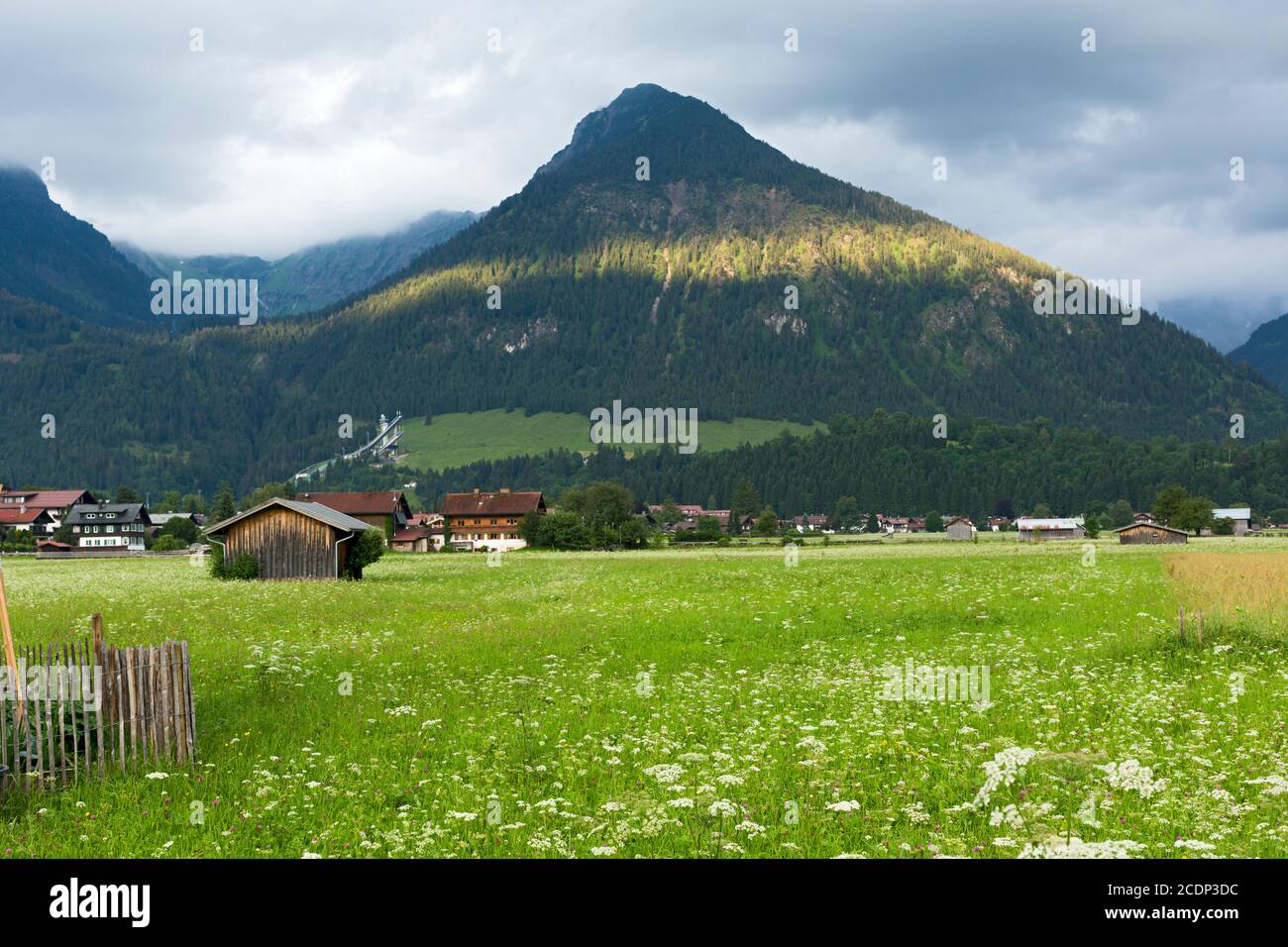 Oberstdorf, Scheune, Häuser, Sprungschanze, bewaldete Berge, Sonnenlicht, tiefliegende Wolken Stock Photo