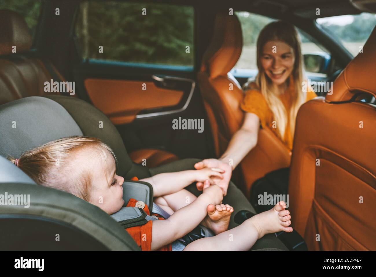 Family child in car holding mother hand baby sitting in safety seat mom driver on road trip vacation travel lifestyle parent with daughter in auto Stock Photo