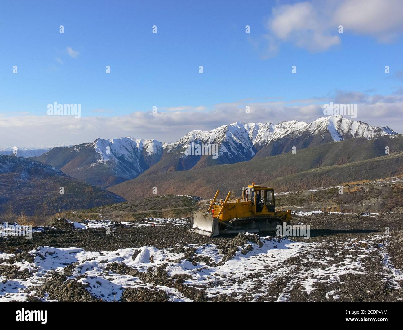 Crawler tractor with grederom against the backdrop of snow-capped mountains Stock Photo