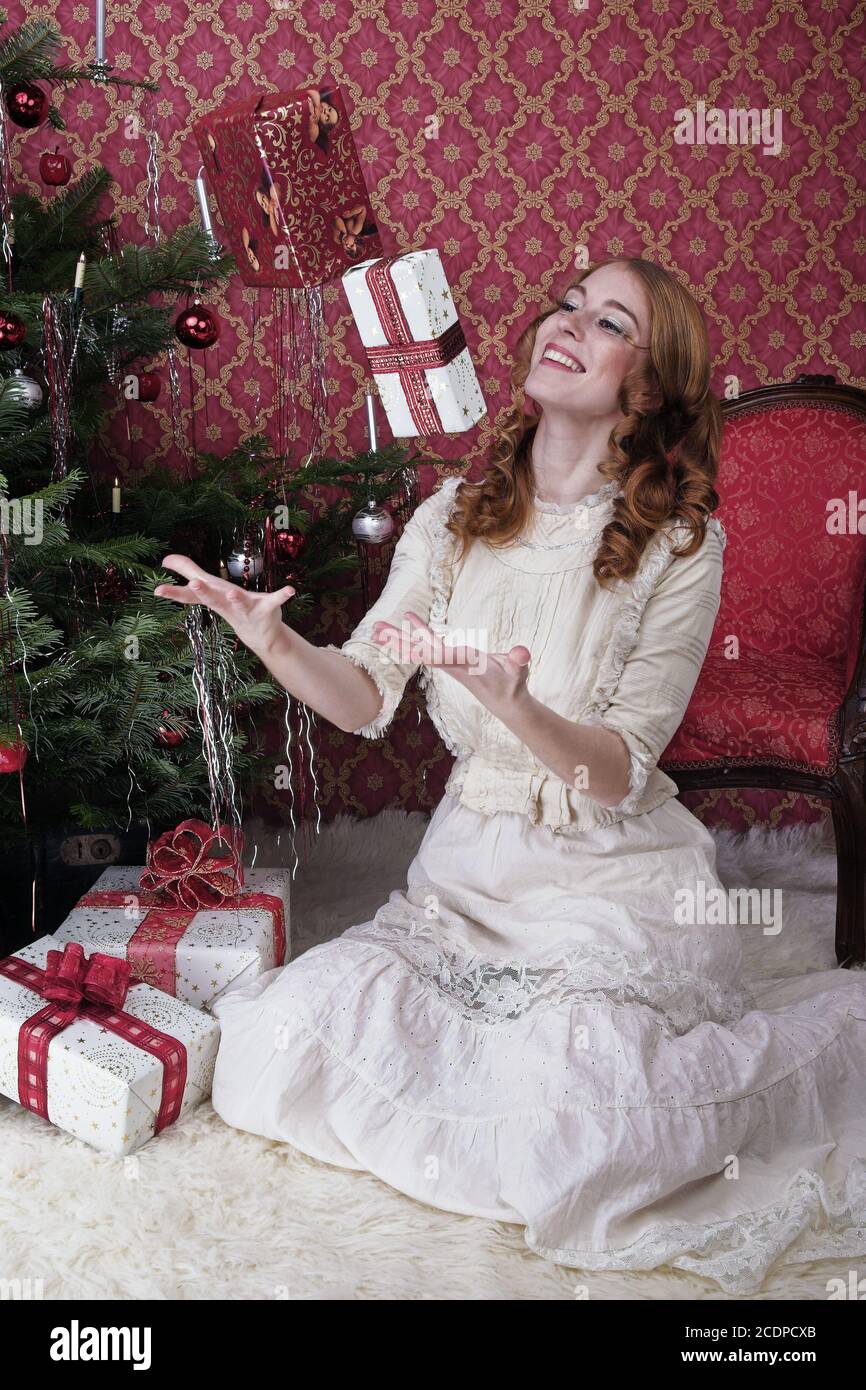 Victorian seeming Christmas scene with young redheaded woman in a antique dress with gift Stock Photo