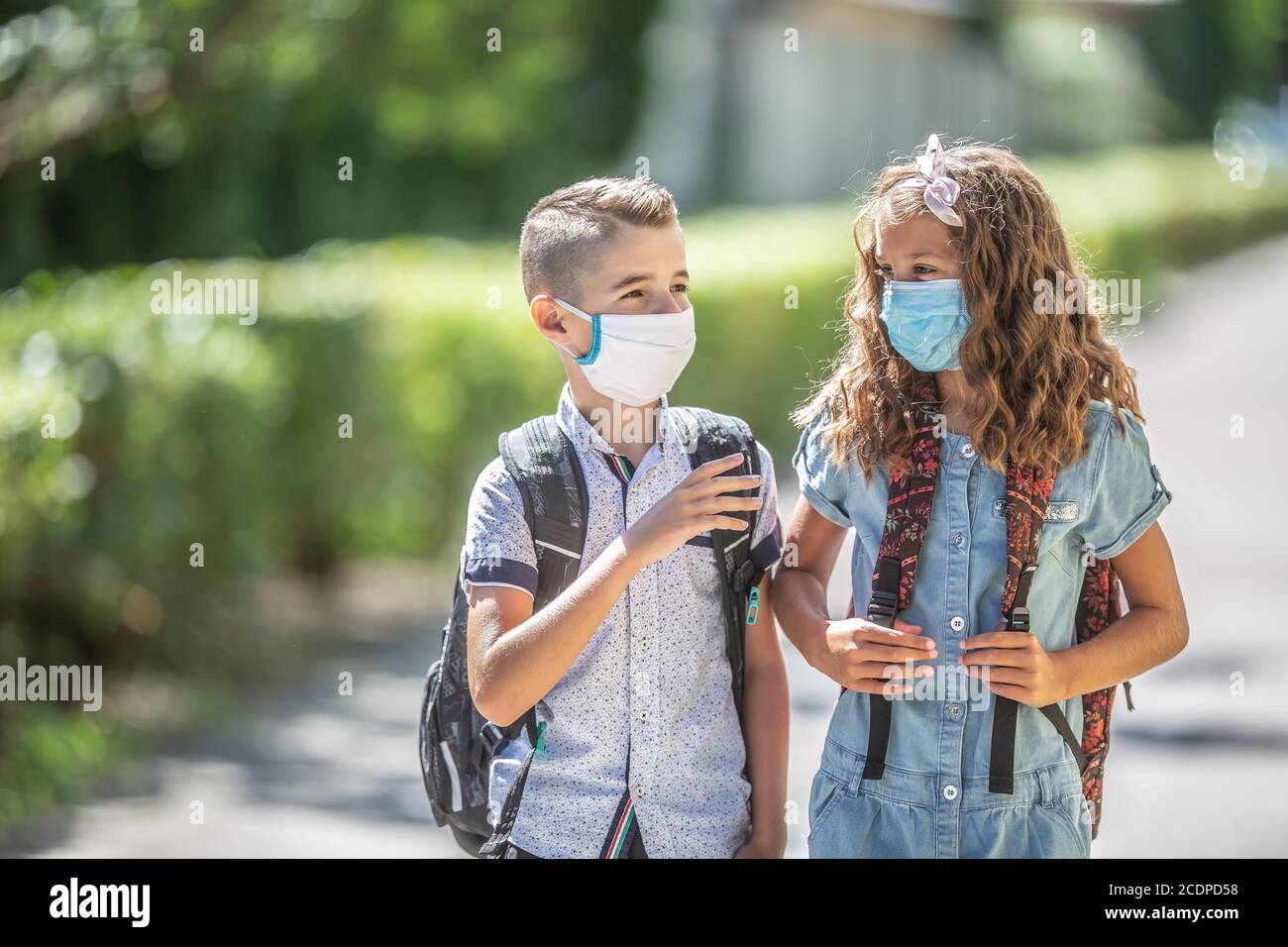Two young friends classmates with face masks talk on their way to school during the Covid-19 quarantine. Stock Photo