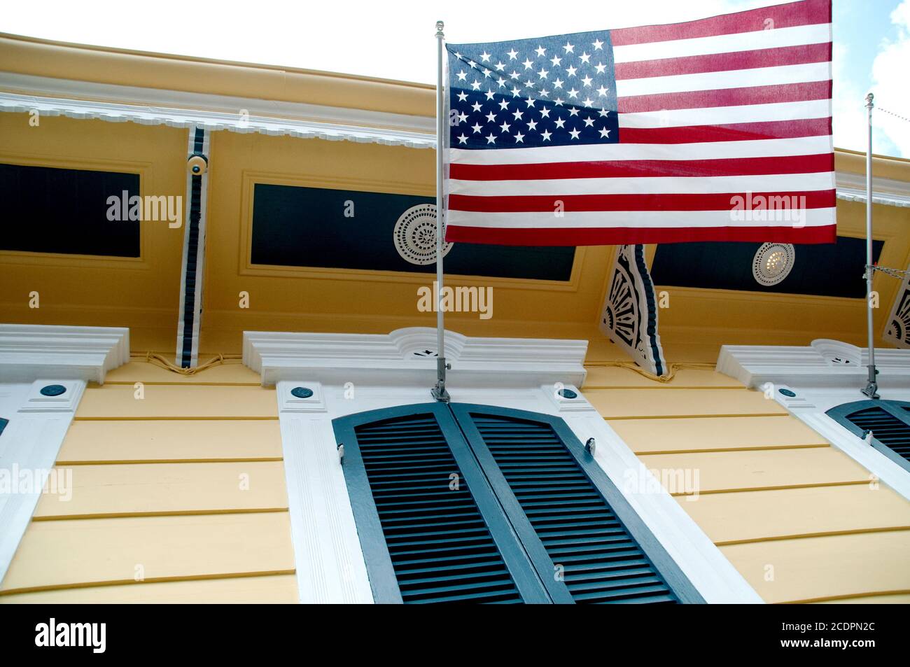 An American flag, the stars and stripes, hanging over the shuttered window of a yellow shotgun house, French Quarter, New Orleans, Louisiana, USA. Stock Photo