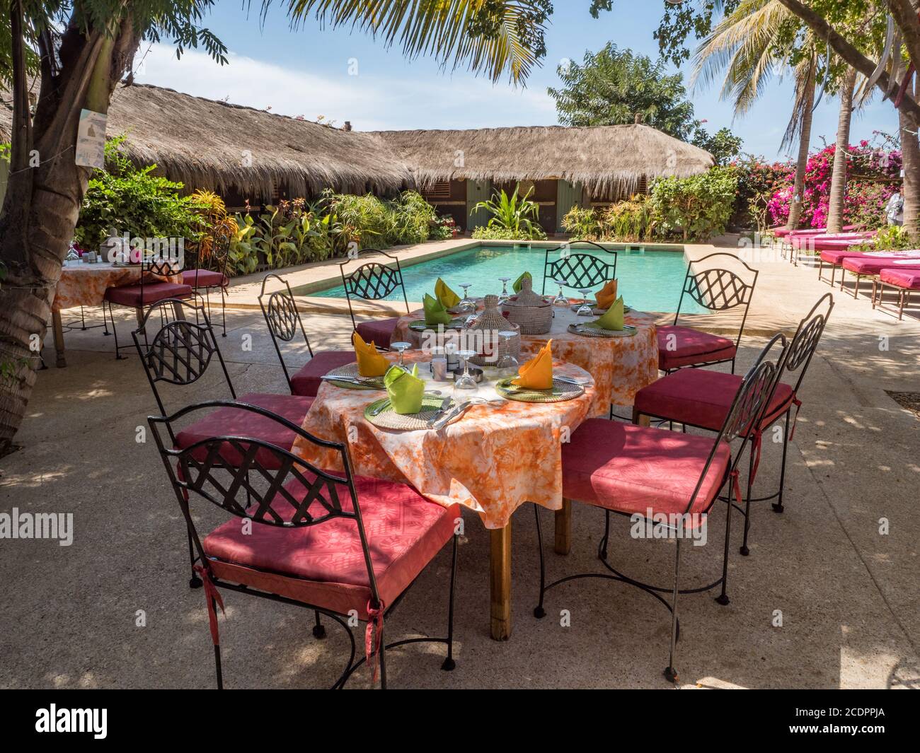 Senegal, Africa - January 2019: A covered table awaits guests next to the pool and African huts with palm leaf roofs. Holiday background. Relaxing vac Stock Photo