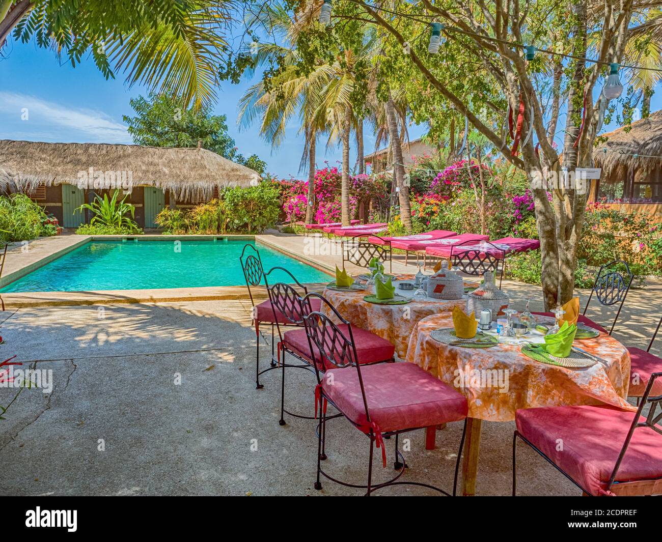 Senegal, Africa - January 2019: A covered table awaits guests next to the pool and African huts with palm leaf roofs. Holiday background. Relaxing vac Stock Photo
