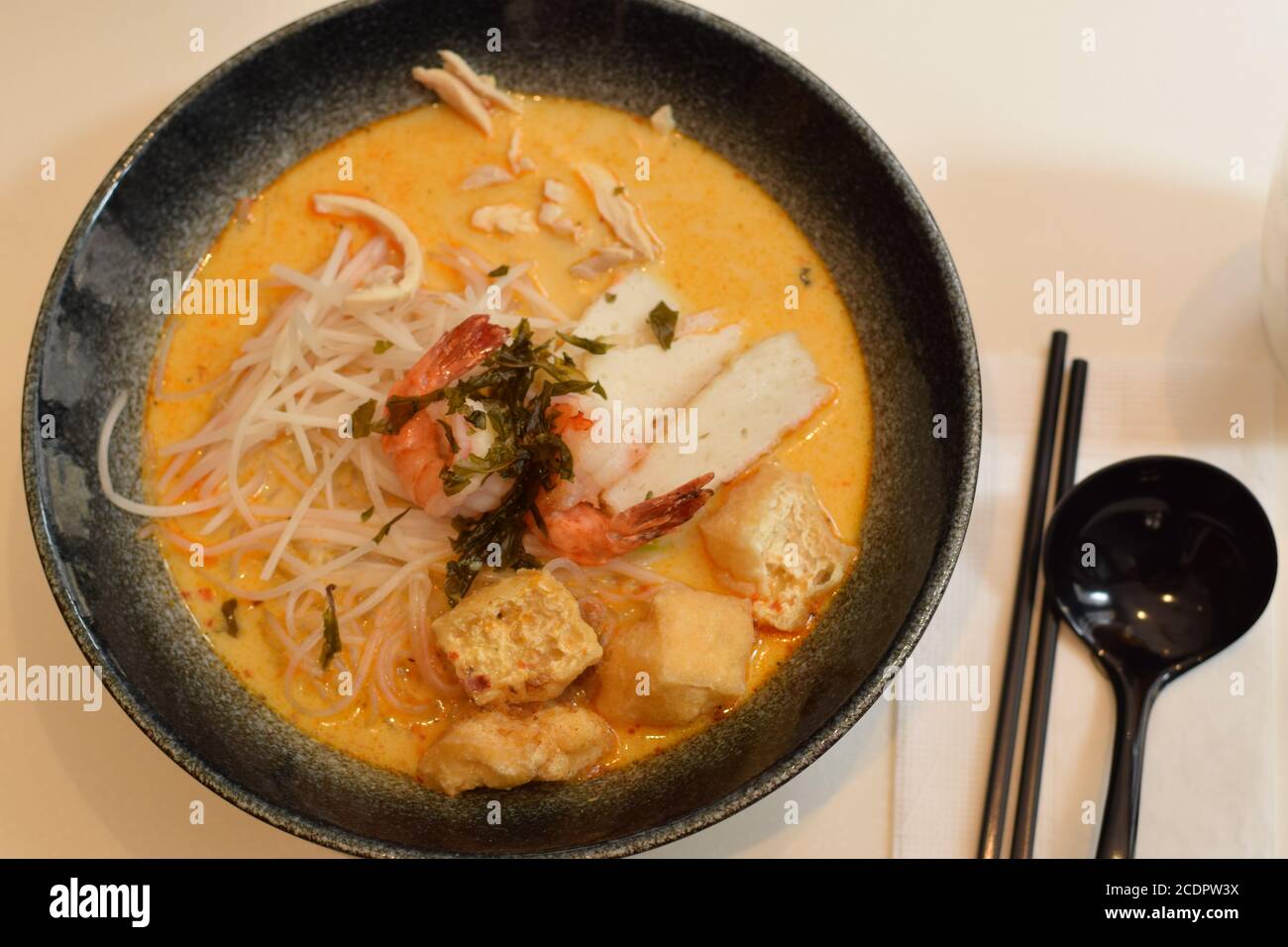 Top view of a bowl of laksa with spoon and chopsticks. Laksa is a typical soup from southeast