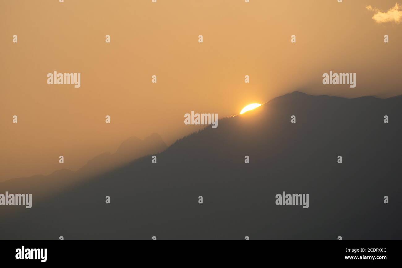 The sun setting behind a mountain and illuminating the whole sky golden ...