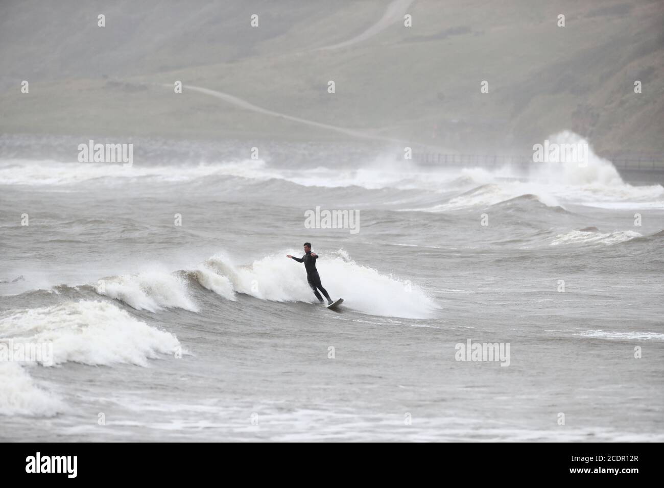A surfer enjoys the rough seas in Scarborough, North Yorkshire. Picture date: Saturday August 29, 2020. Forecasters predict this Bank Holiday Monday could be the coldest on record for some parts of the UK as temperatures are expected to be well below average for the time of year. See PA story WEATHER Thunderstorms. Photo credit should read: Danny Lawson/PA Wire Stock Photo