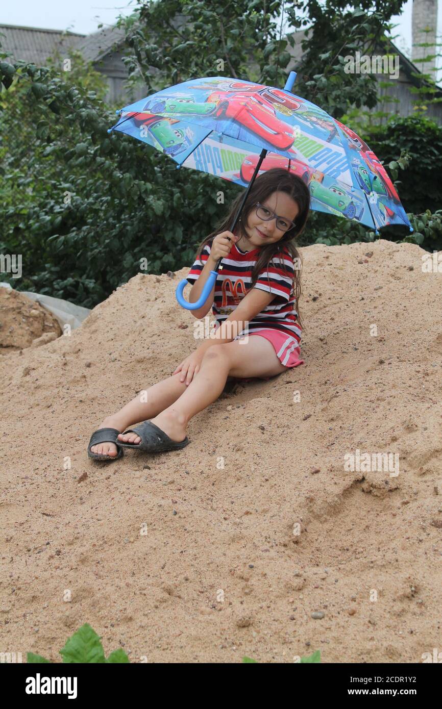 girl under bright umbrella play under rain  in the garden in last summer day on vacation Stock Photo