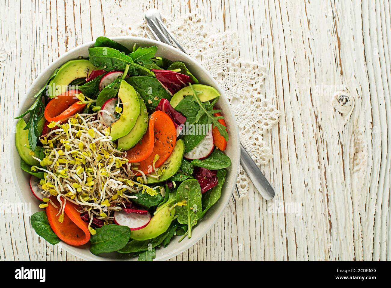 Healthy green salad with alfalfa sprouts, avocado and fruit on wooden background Stock Photo