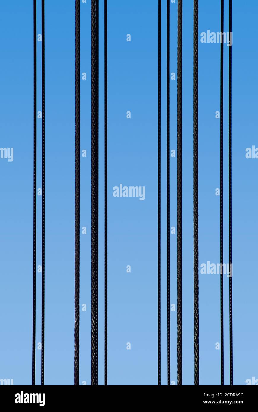 Parallel vertical steel ropes before a blue sky. Stock Photo