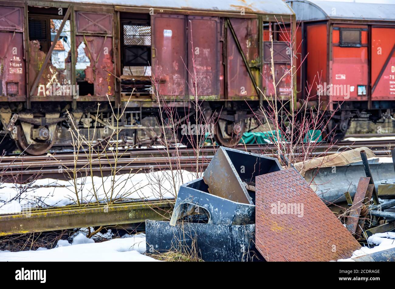 Dirty old rusty wrecked freight card on a siding with scrap metal in front in winter. Stock Photo