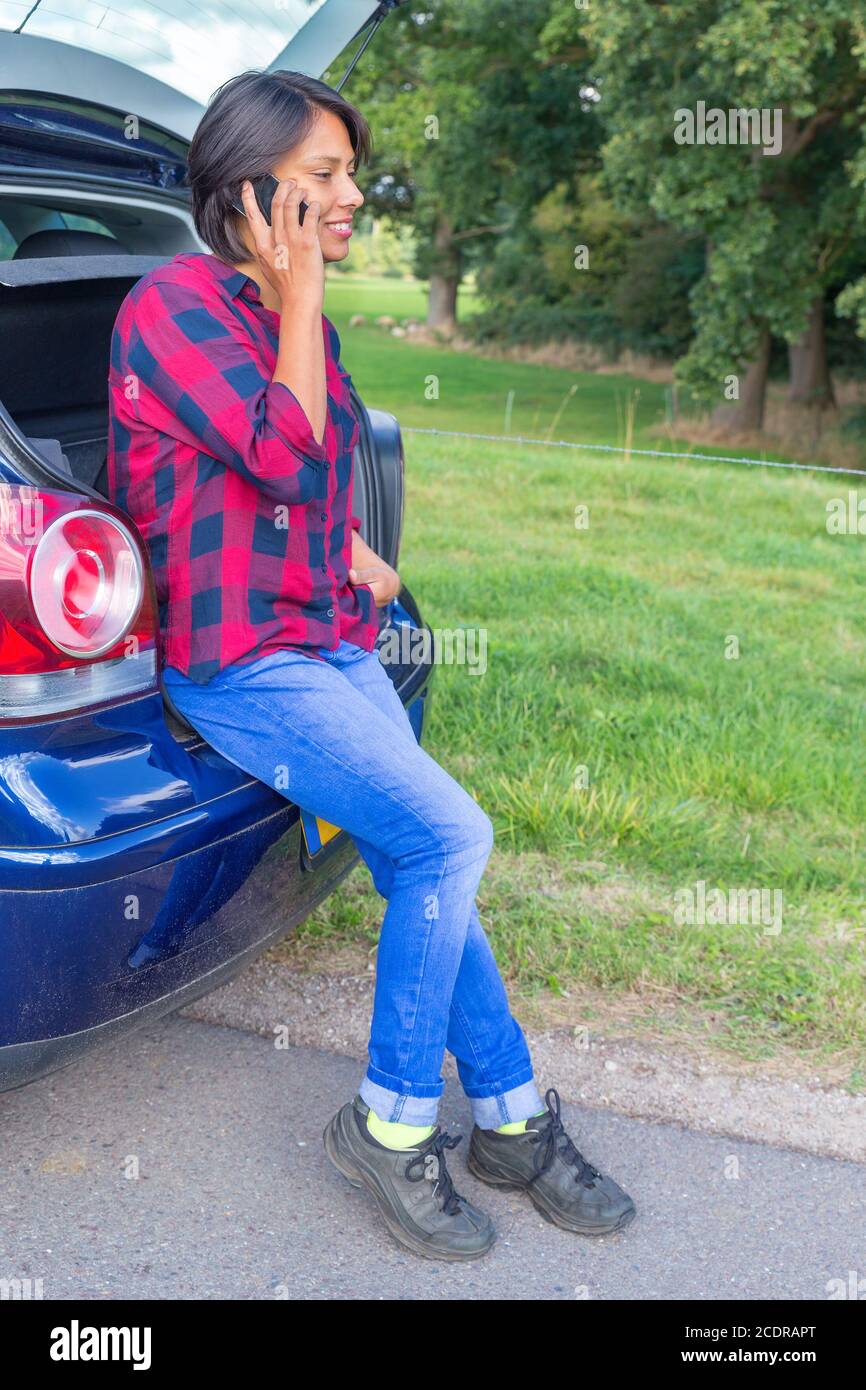 Woman phoning mobile sitting in car trunk outside Stock Photo