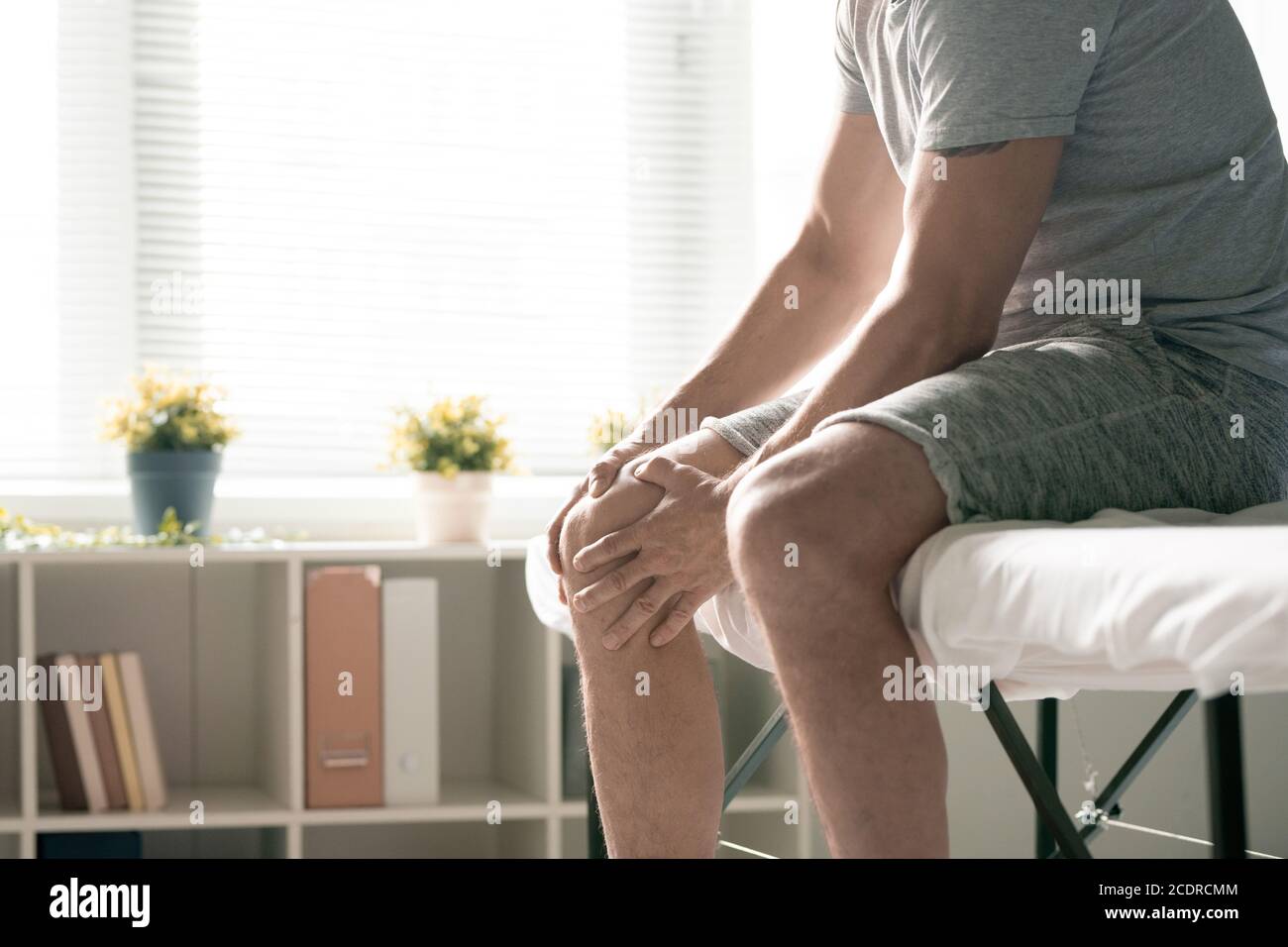 Contemporary sportsman in activewear massaging right knee of injured leg Stock Photo