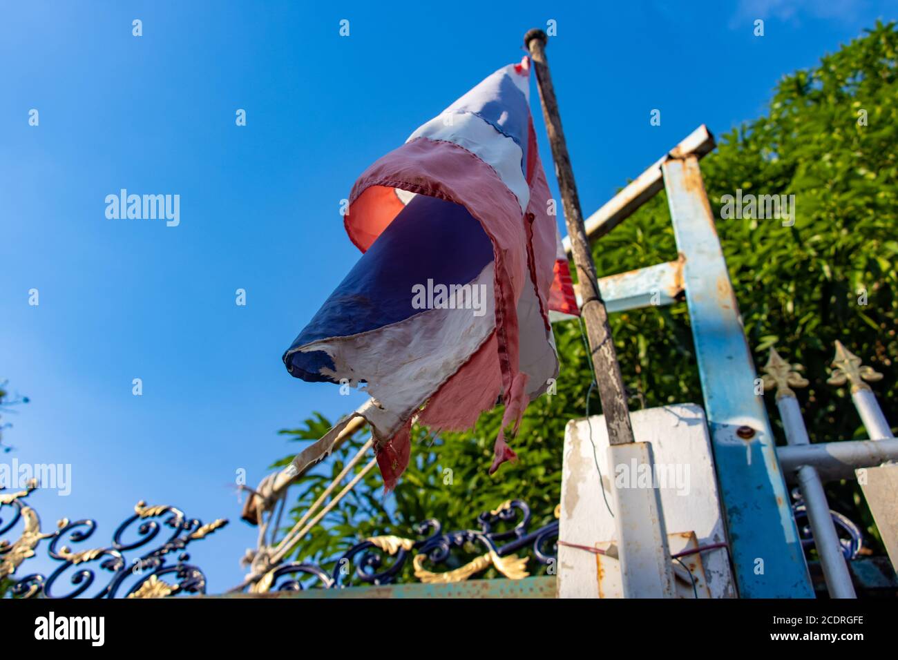 The torn flag of the Kingdom of Thailand fluttering on the fence, view from below. Stock Photo
