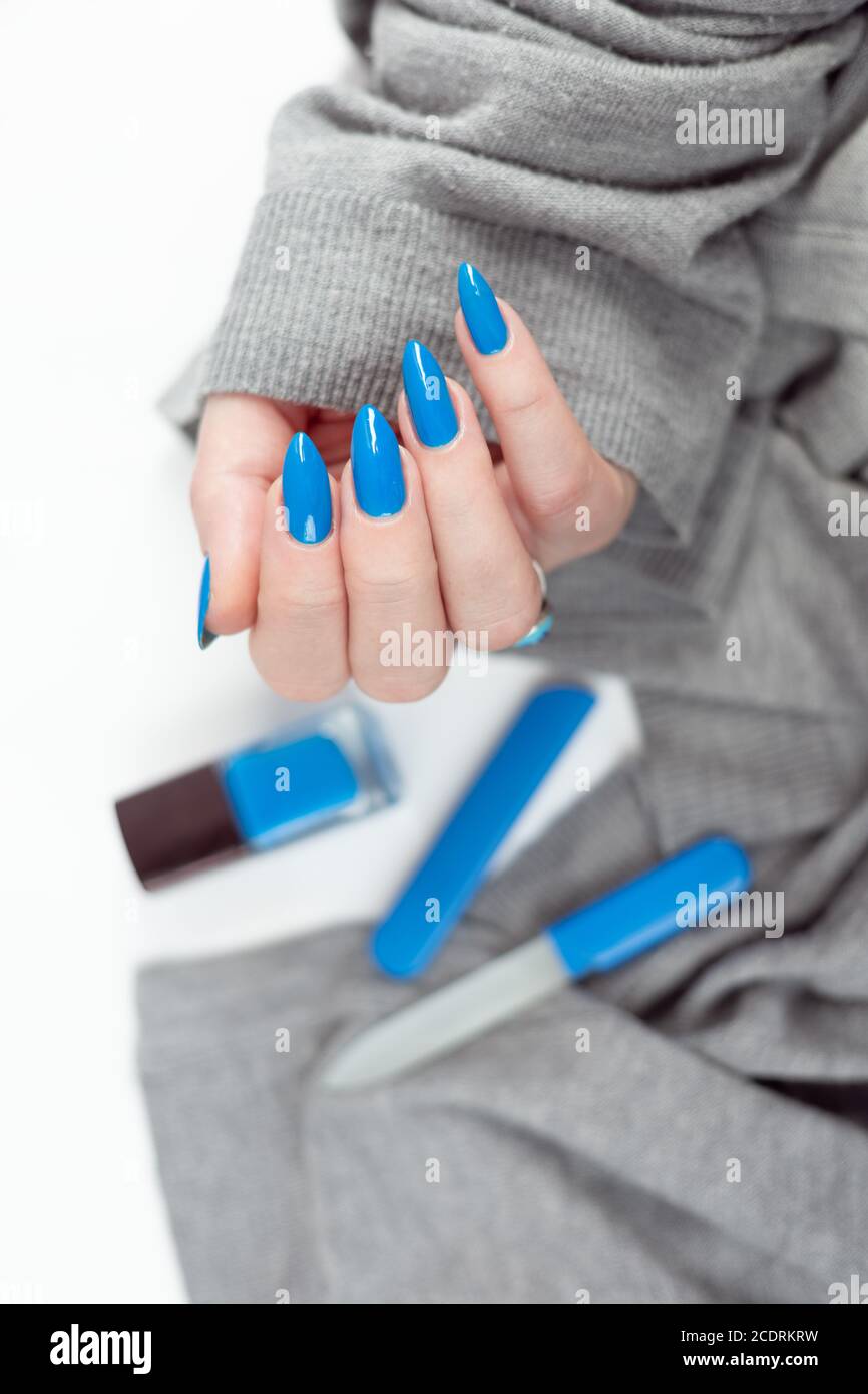 Female hand with long nails and light blue manicure with bottles of nail  polish Stock Photo - Alamy