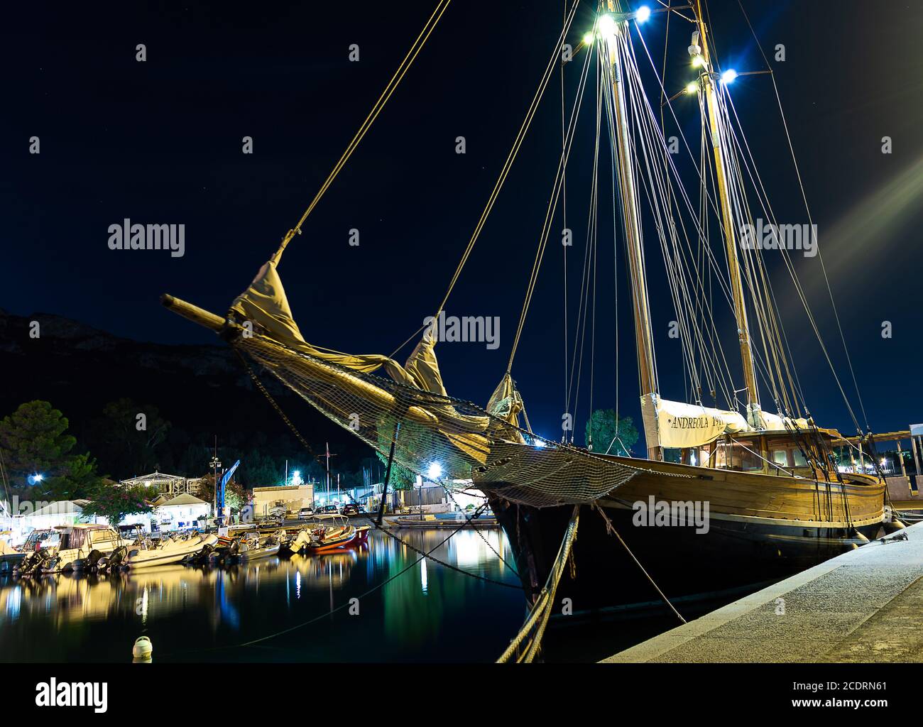 Cagliari, Sardinia, Italy - August 28 2020: vintage old wooden sailing vessel ship moored to city pier on mediterranean sea coast at night Stock Photo
