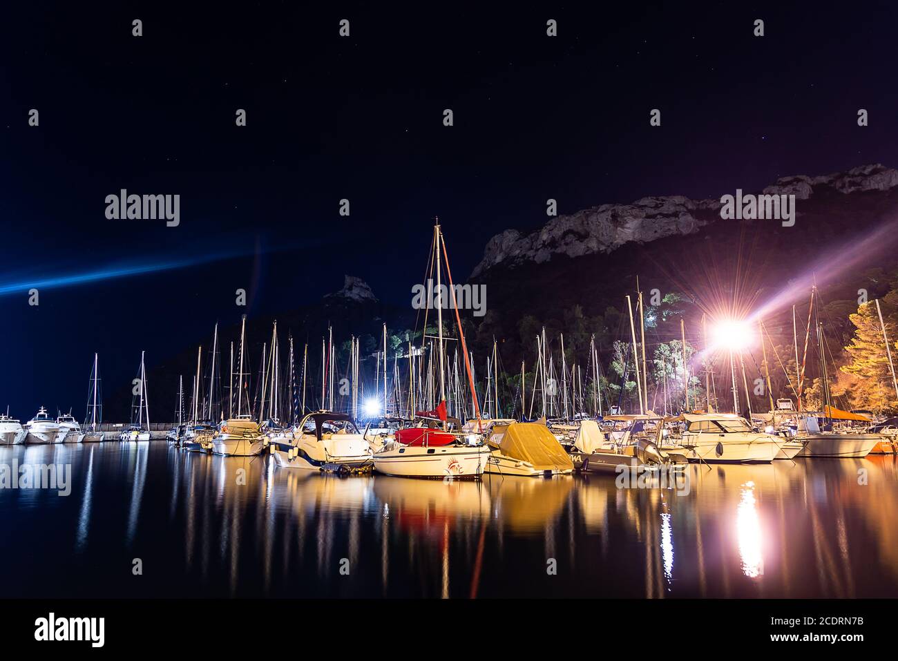 Cagliari, Sardinia, Italy - August 28 2020: lots of boats moored at city pier at night, with water reflections and lights - Sella del diavolo on backg Stock Photo