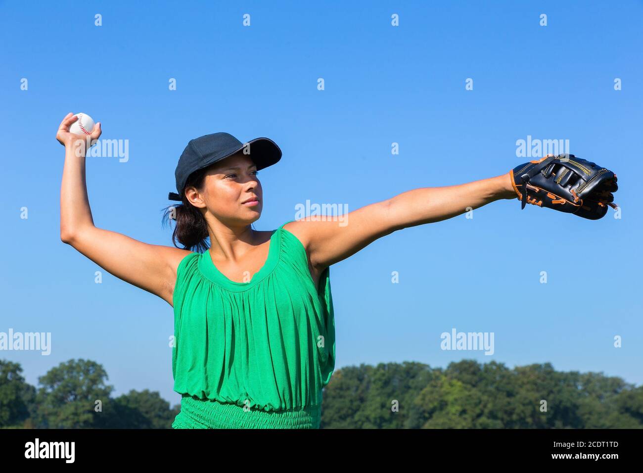 Woman with glove and cap throwing baseball outside Stock Photo