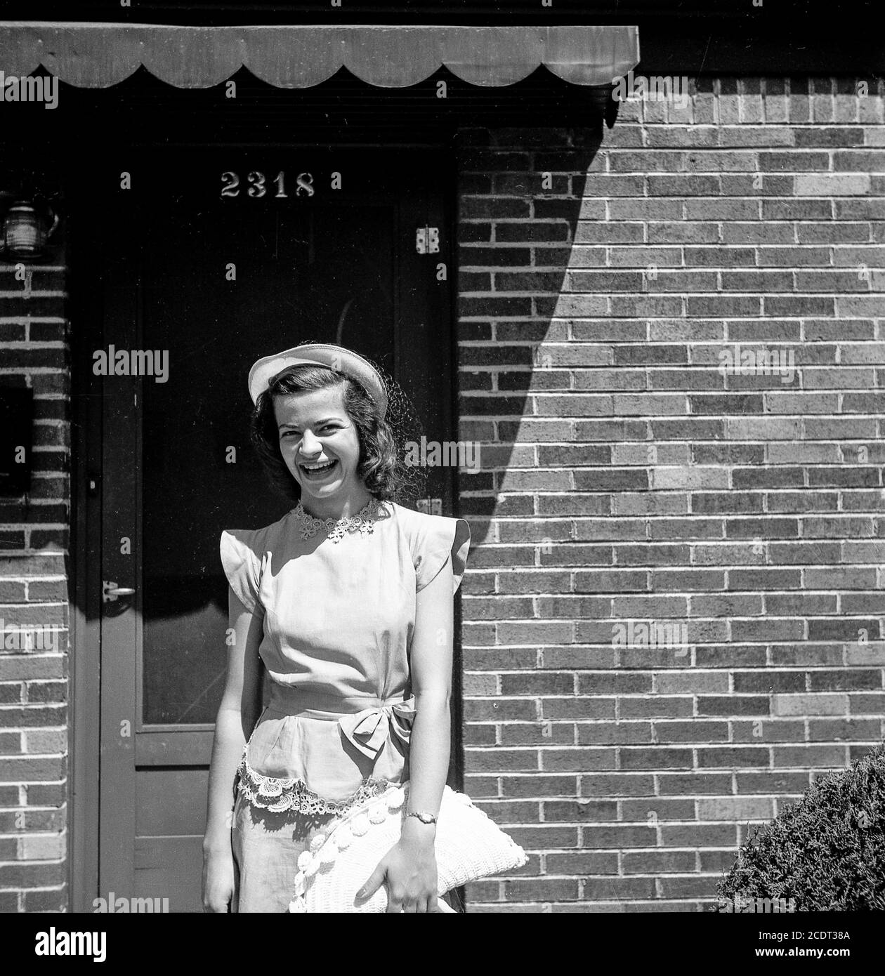 Pretty young woman poses in Sunday best in front of a residential home, U.S.A.  1940s Stock Photo