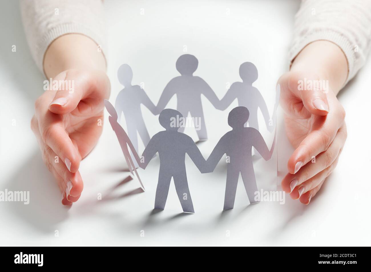 Paper people surrounded by hands in gesture of protection. Concept of insurance Stock Photo