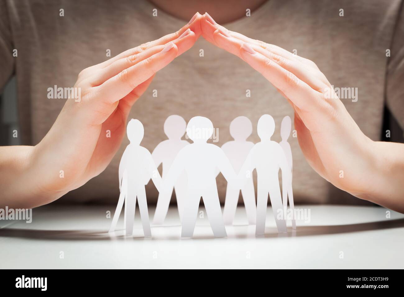 Paper people under hands in gesture of protection.. Concept of insurance Stock Photo