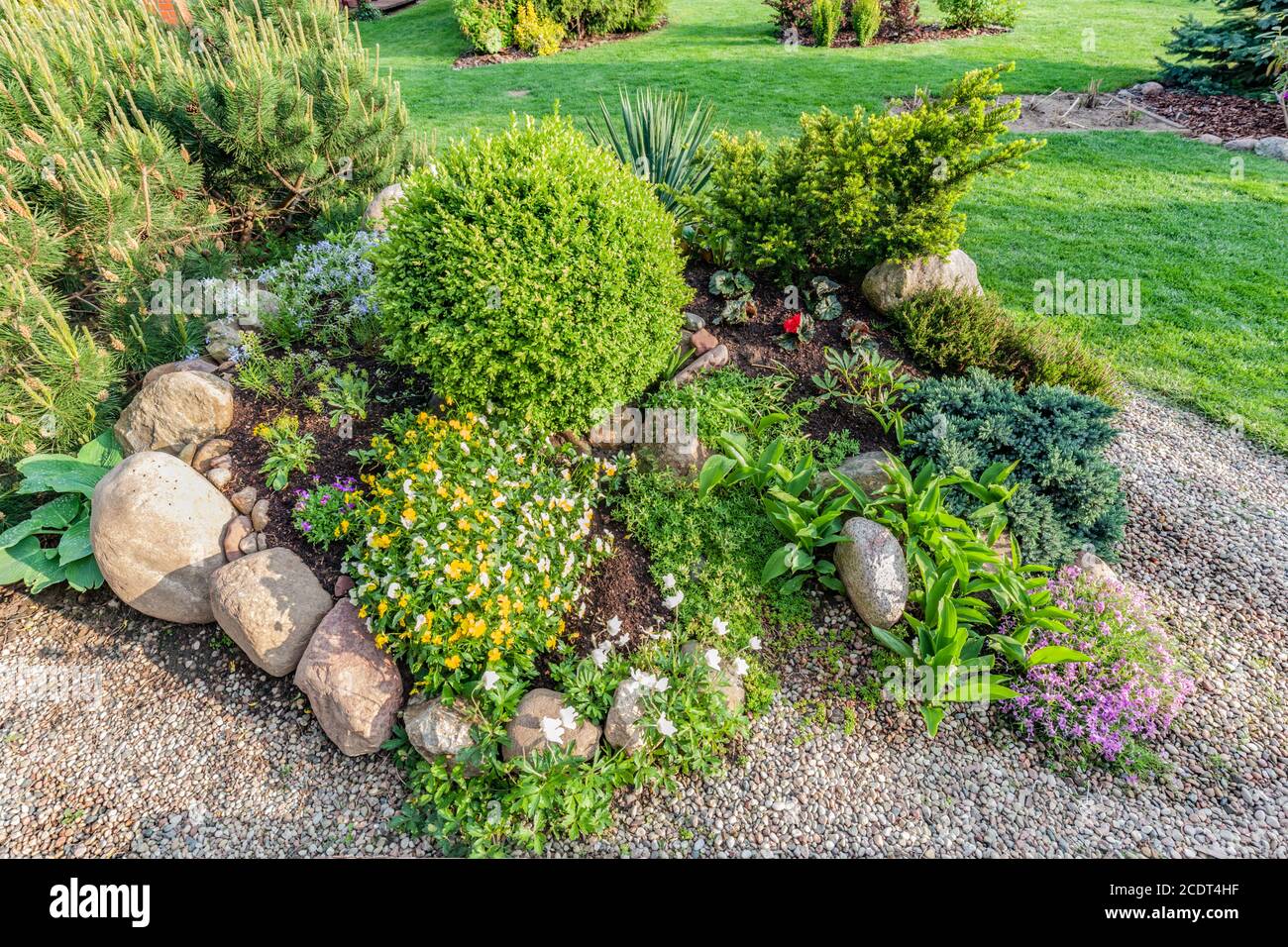 Landscaped summer garden with green plants, rocks, flowers in flowerbeds, mown grass. Stock Photo