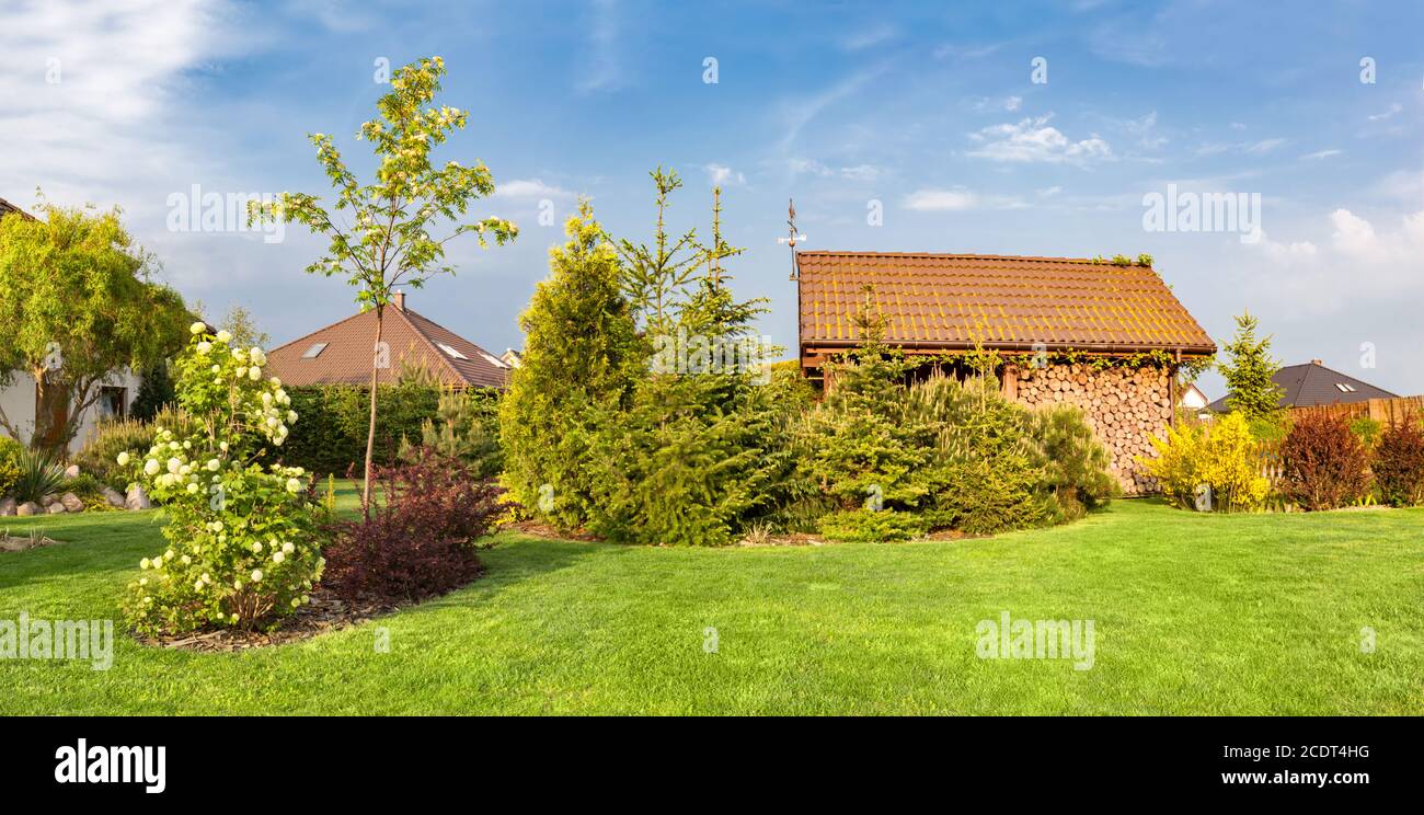 Backyard of a family house. Landscaped garden with green mown grass, wood shelter. Stock Photo