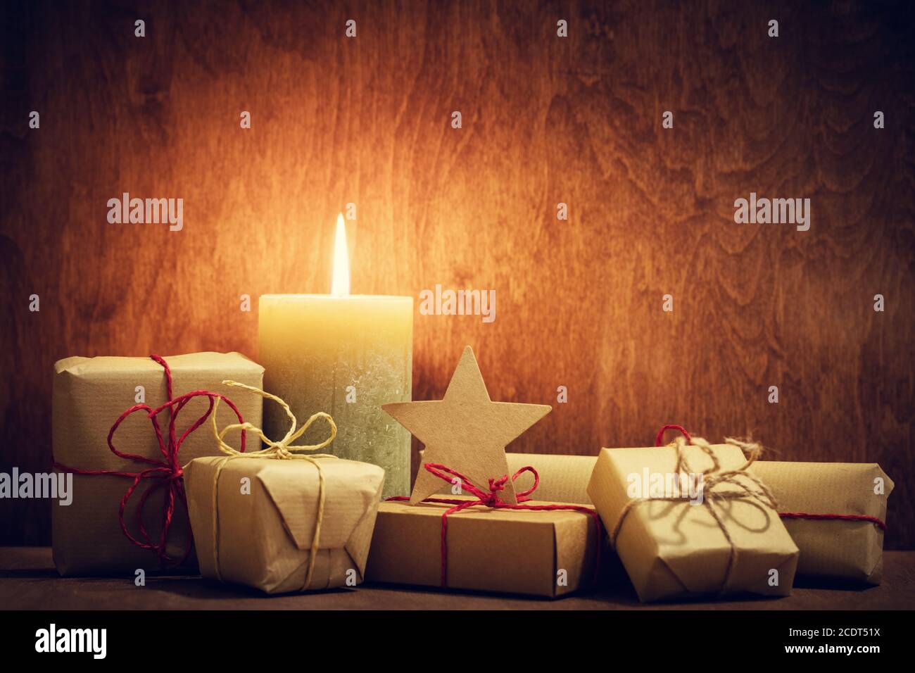 Chistmas presents, gifts with a candle glowing on wooden wall background. Stock Photo