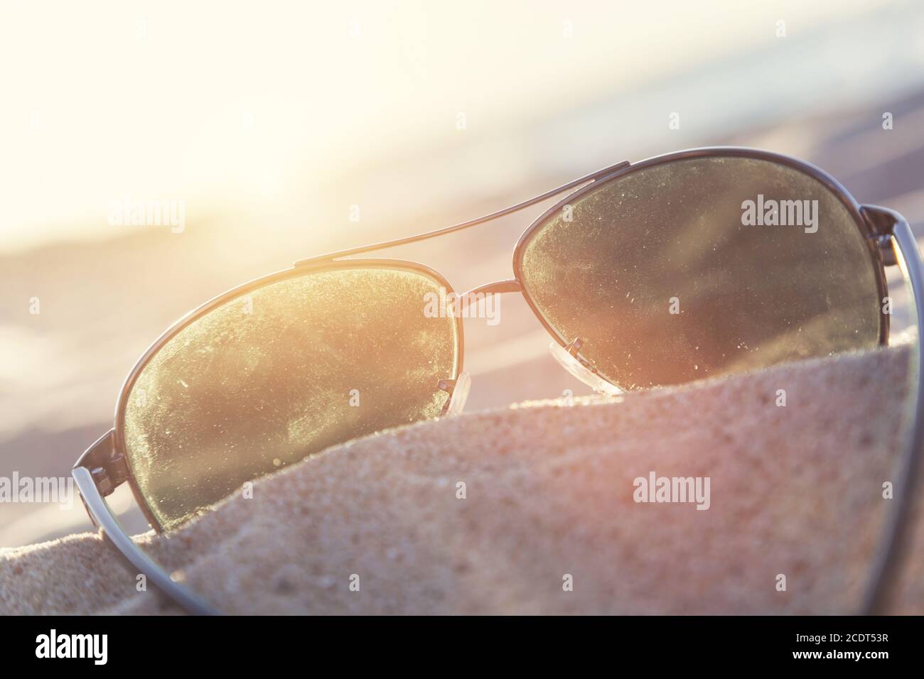 Sunglasses on sand at sunset, beach and ocean in the background. Stock Photo