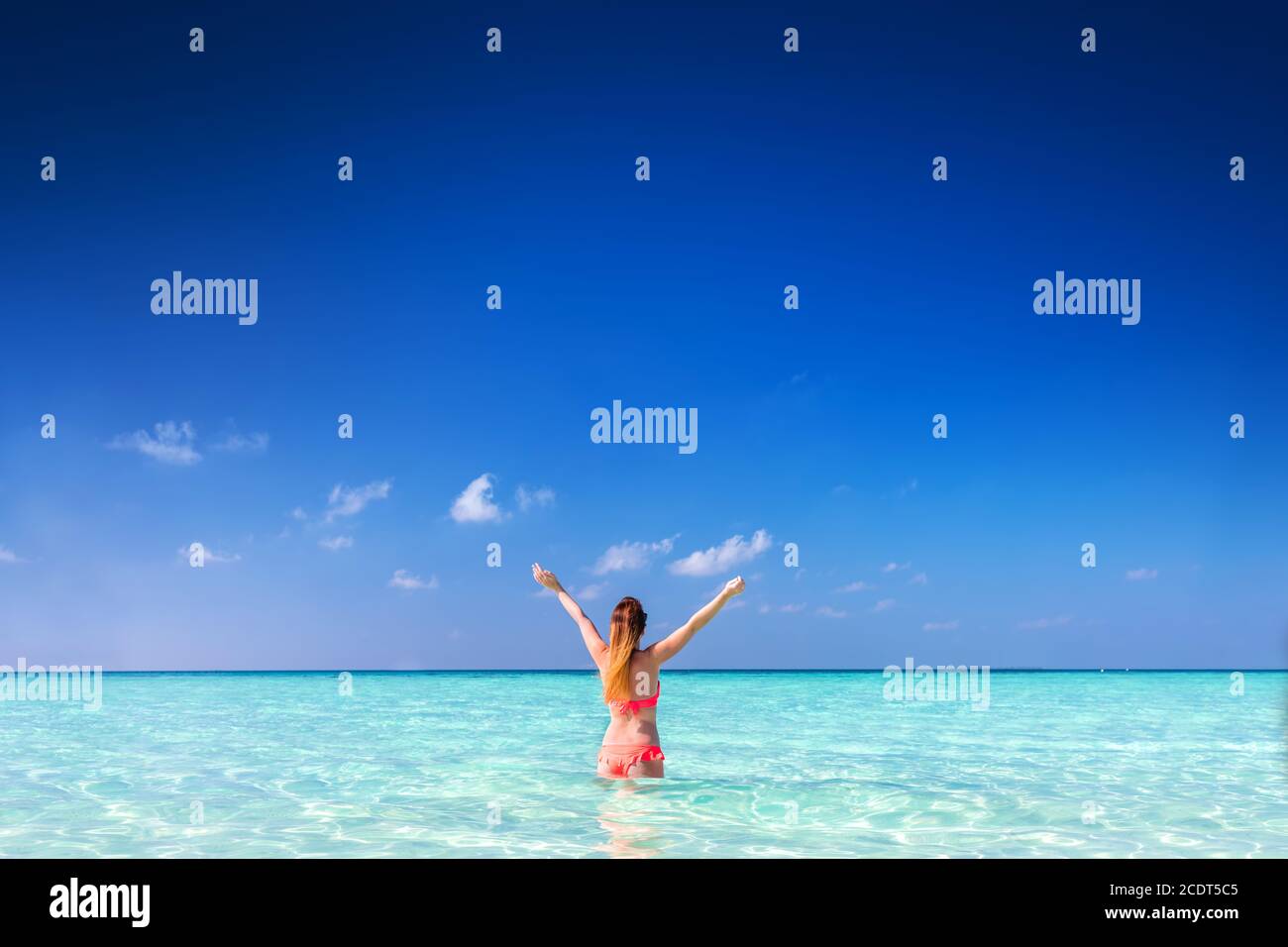 Beautiful young woman standing in the ocean with hands raised. Maldives Stock Photo