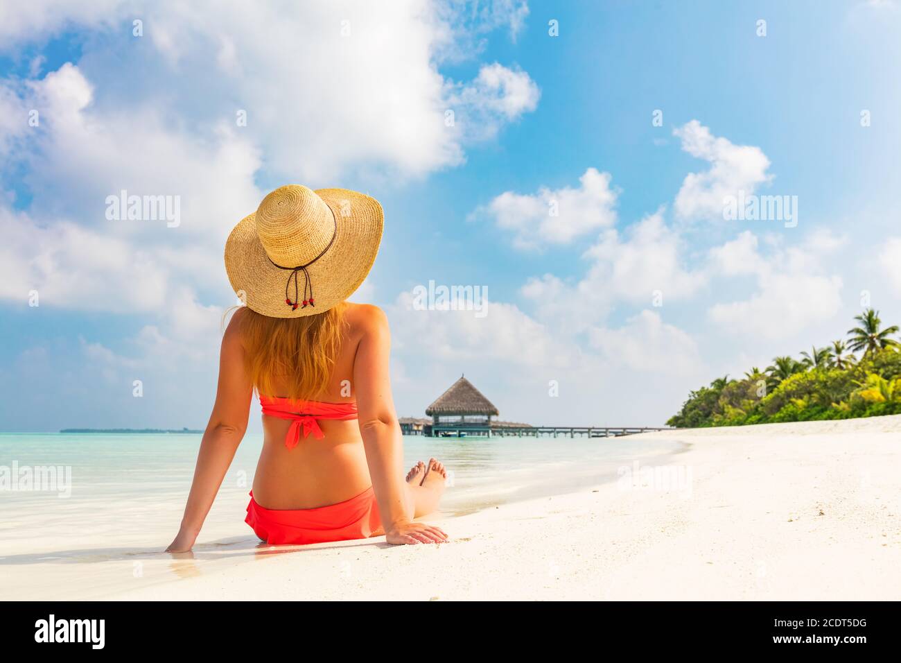 Beautiful young woman in sunhat sitting relaxed on tropical beach in Maldives Stock Photo