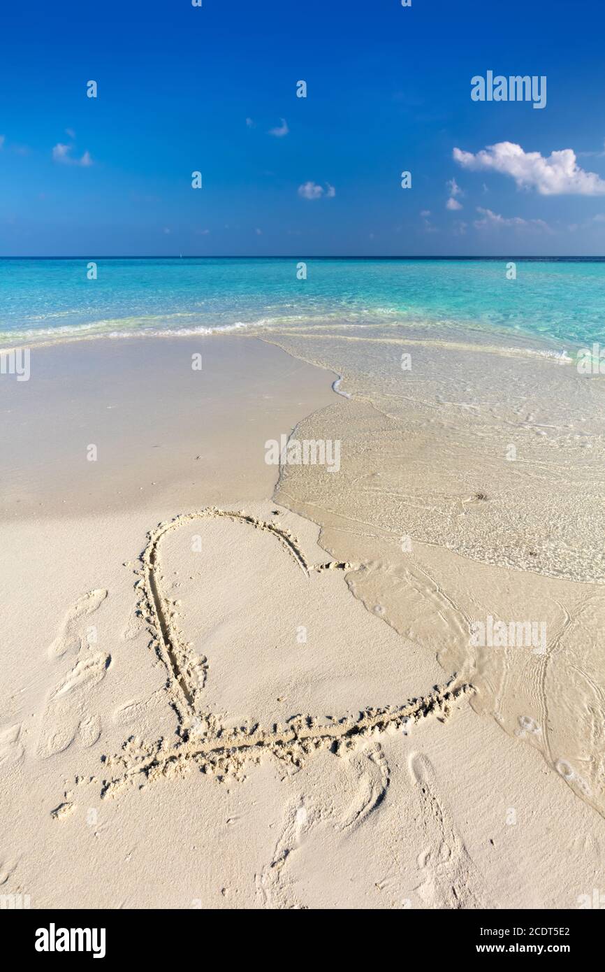 Waves wash away a heart drawn on sand of a tropical beach Stock Photo